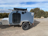 Grey off-road teardrop camper ready for your RV rental mountain adventure. Features diamond plate storage & roof rack.