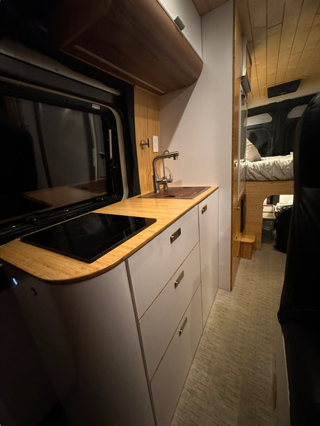 Step inside this modern RV rental! Features a sleek kitchen with sink & induction cooktop, plus a cozy sleeping area.