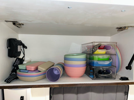 RV rental organization: Pastel kitchenware (bowls, cups, containers) & electronics neatly stored in a compact cabinet.