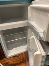 Clean, empty compact RV rental refrigerator. Inside features a freezer, clear shelves, and crisper drawer.