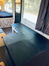 Spacious pop-up RV rental interior featuring dark cushioned benches, a bed, and bright windows for a cozy camp.