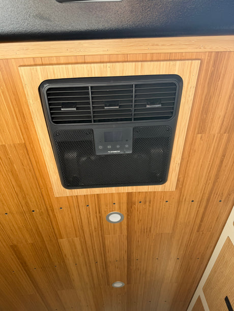 Overhead Dometic AC unit installed in a light bamboo ceiling of an rv rental, providing air conditioning for the van interior.