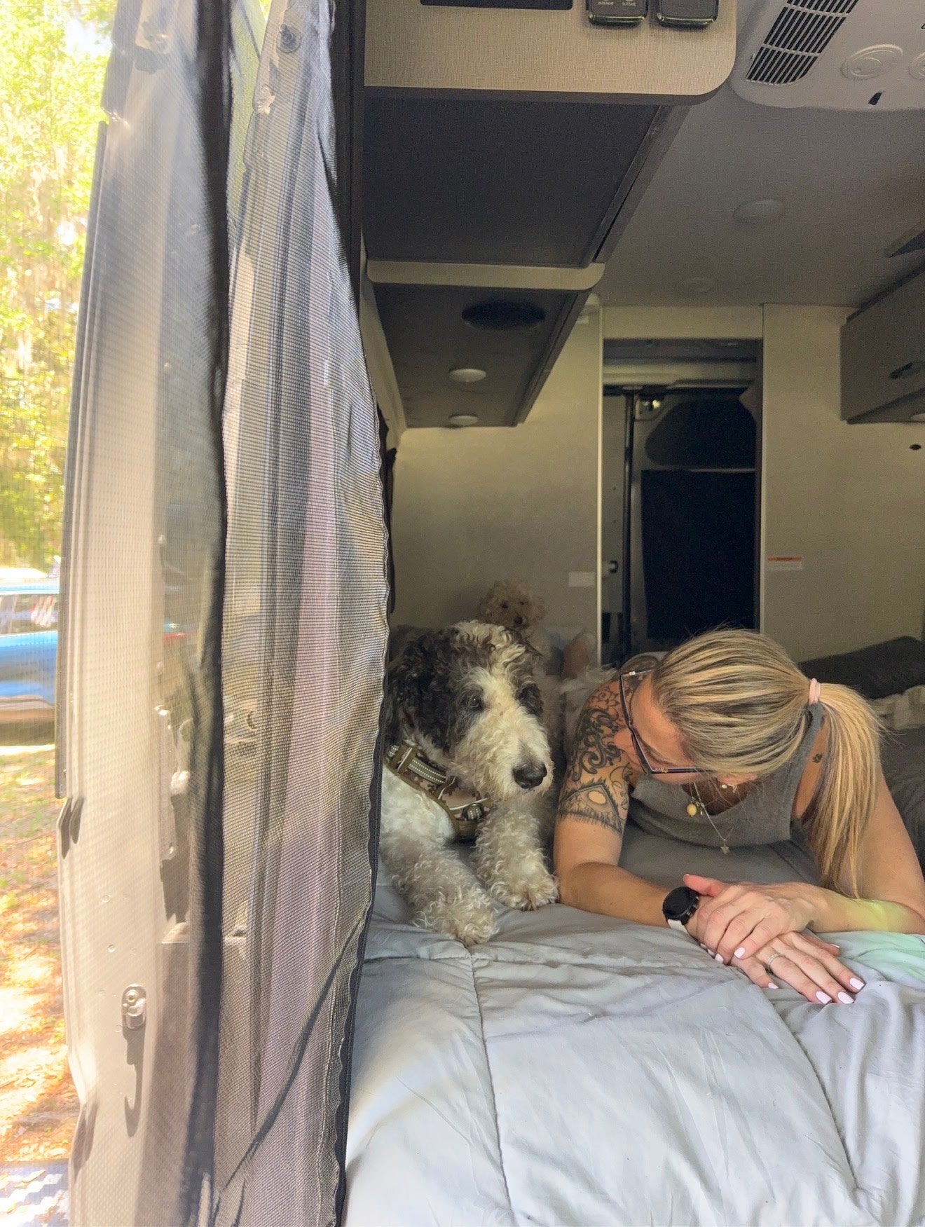Relaxing inside an RV rental with my furry companions. A woman and two dogs enjoy downtime, looking out at nature.