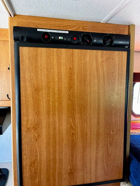 RV rental refrigerator: A wood-paneled fridge with a top control panel inside an RV. Ideal for compact living.