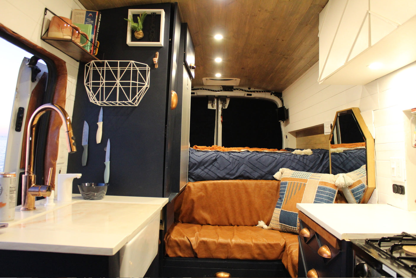 Inside this modern RV rental: sleek kitchenette with copper faucet, comfy bench, and a cozy rear bed area.