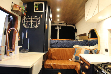 Inside this modern RV rental: sleek kitchenette with copper faucet, comfy bench, and a cozy rear bed area.