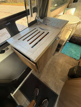 Compact RV rental kitchen with a sleek sink, integrated drainer, and cozy dining nook. Tiled floor adds comfort.