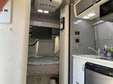 RV rental: well-appointed interior showing bedroom with TV, and kitchen with sink, microwave, Dometic fridge.