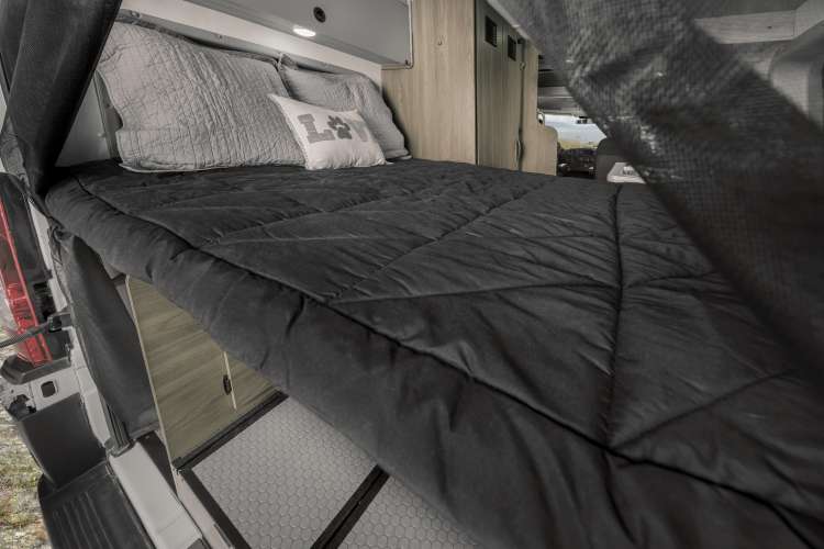 Comfortable RV rental bed setup with black comforter, gray pillows, interior storage, and unique hexagonal flooring.