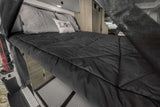 Comfortable RV rental bed setup with black comforter, gray pillows, interior storage, and unique hexagonal flooring.