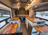 Modern camper van interior: a cozy bed, well-equipped kitchen, and fold-out tables, ideal for an RV rental.