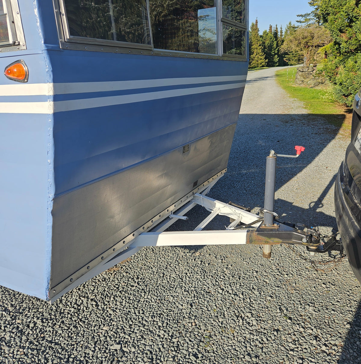 Light blue RV rental trailer, featuring white stripes, hitched to a car on a sunny gravel driveway. — photo 17