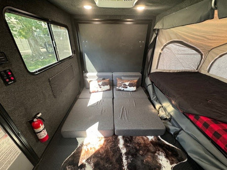 Inside an RV rental: flexible grey mattresses, a pop-up tent bed, and a decorative animal print rug.