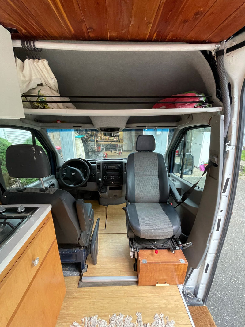 Interior of a converted rv rental camper van, showing a kitchen, swiveling front seats, wooden floors, and overhead storage. — photo 12