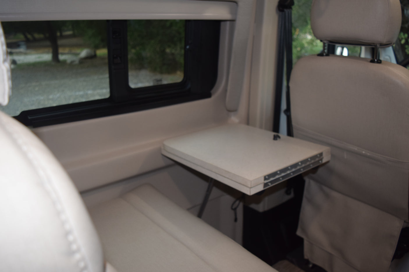 RV rental interior: A light-colored, fold-out table is set between plush seating, with a clear view outside a window.