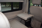 RV rental interior: A light-colored, fold-out table is set between plush seating, with a clear view outside a window.