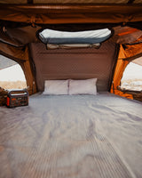 Cozy rooftop tent bed setup for your next RV rental adventure. Features a power station, pillows, and expansive desert views.