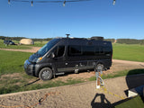 Dark gray RV rental parked at a scenic campground with hookups and a glamping tent in the background.