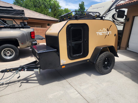 Rugged tan Teton teardrop trailer RV rental, hitched to a grey GMC dually truck in a driveway. Ready for camping.