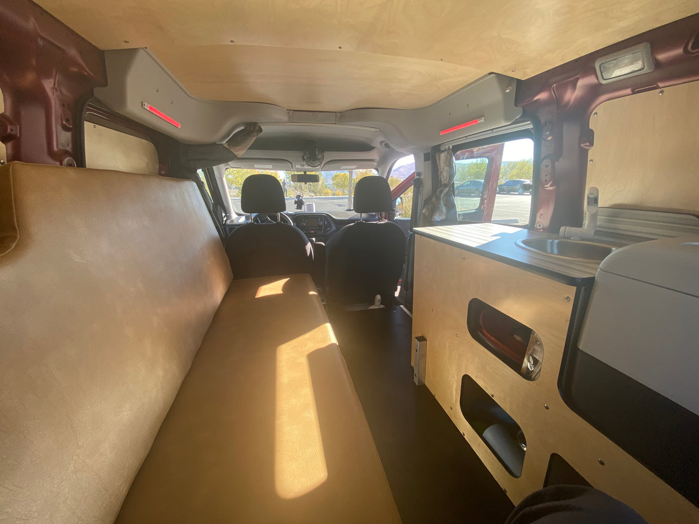 Inside an RV rental: view from rear showing a long bed on left & a kitchenette on the right. Custom ceiling & storage.