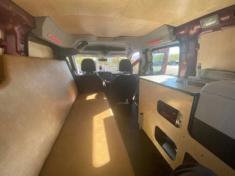 Inside an RV rental: view from rear showing a long bed on left & a kitchenette on the right. Custom ceiling & storage.