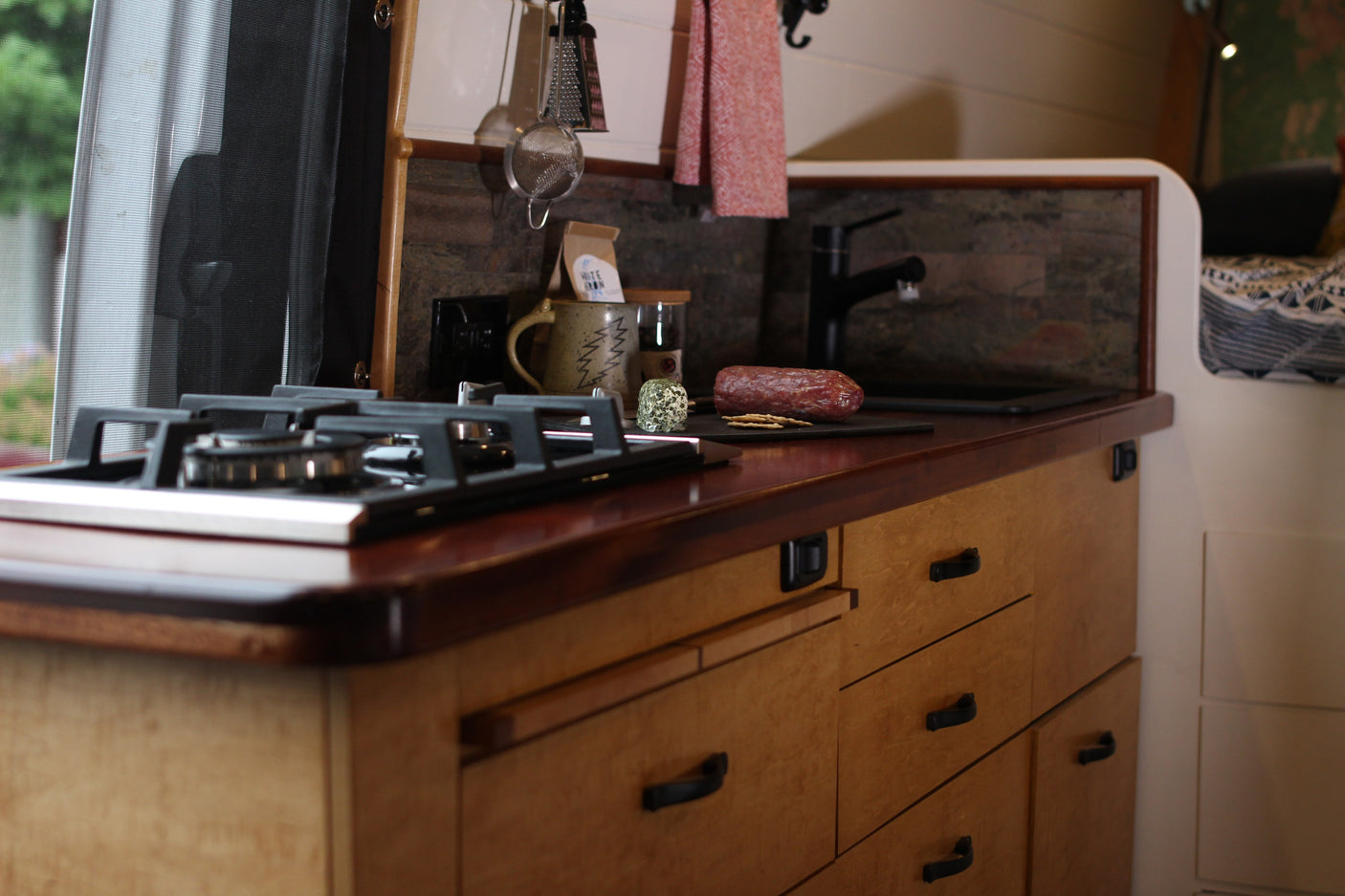 Inside an RV rental: a modern kitchen with a gas stove, wood counter, sink, and a charcuterie setup, ready for adventure.