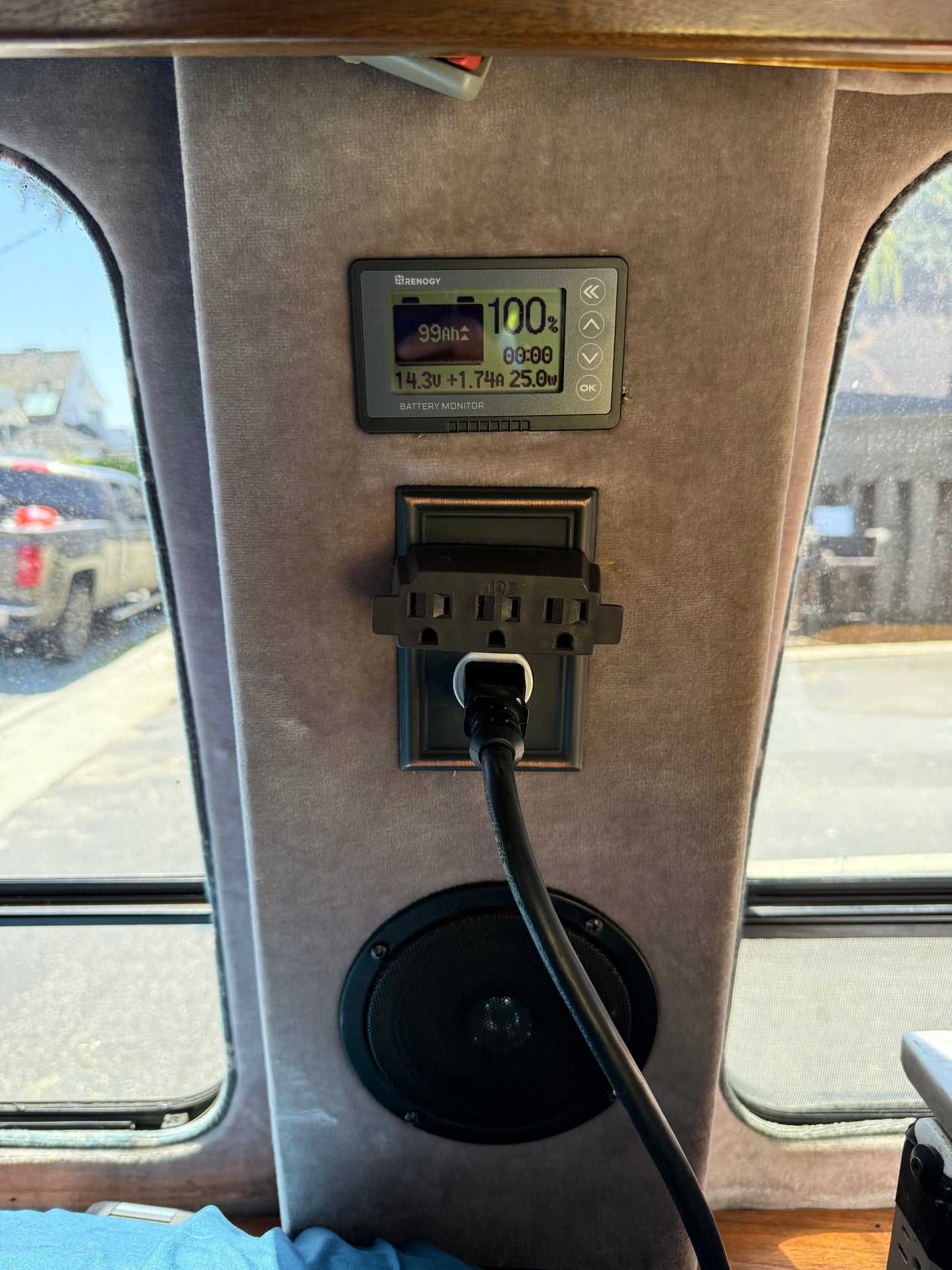Inside an **rv rental**: Renogy battery monitor (100% charged), AC power outlet with cord, and a speaker. Essential mobile power setup.