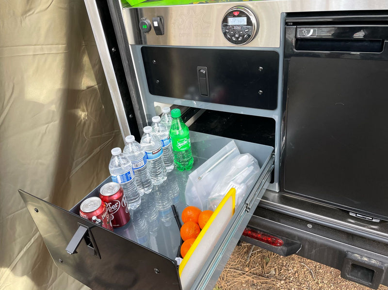  & amenities for your rv rental camping adventure in the pine forest.|Off-road ready RV rental: A white FJ Cruiser tows a black overland trailer in a dense pine forest setting.|This RV rental features an accessible outdoor kitchen pull-out drawer with drinks — photo 7