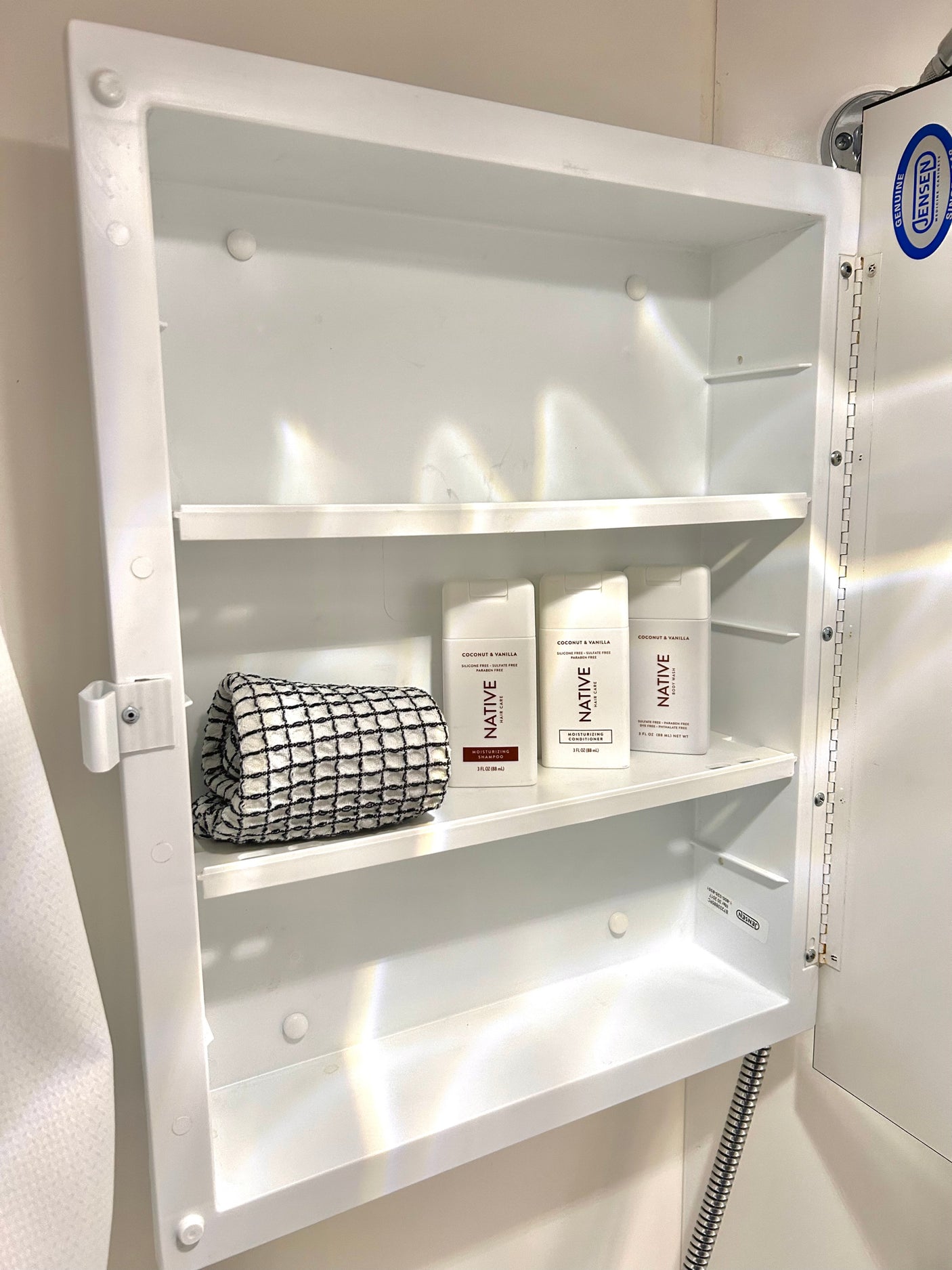 Compact white medicine cabinet in an RV rental, stocked with travel-sized Native brand toiletries & a towel. Jensen cabinet.