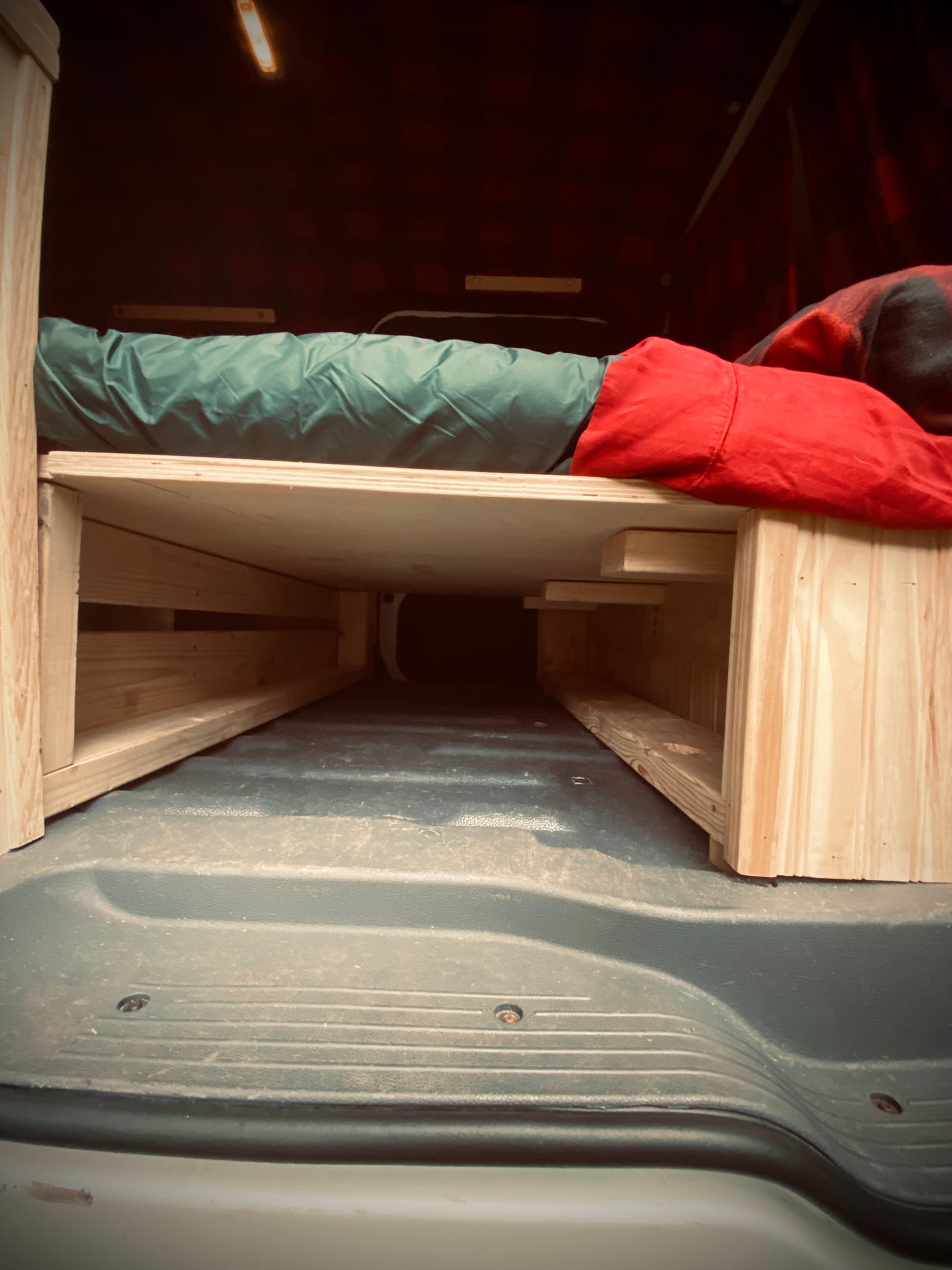 RV rental interior: A DIY wooden bed platform with green and red bedding provides cozy sleeping space above ample storage.