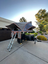 A Roofnest rooftop tent on a camping trailer, fully set up in a driveway. An ideal rv rental for outdoor adventures.