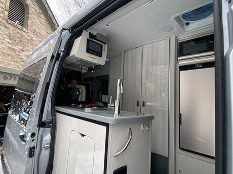 Step inside this RV rental! A compact kitchen with sink, stovetop, microwave, and fridge, ready for snowy adventures.