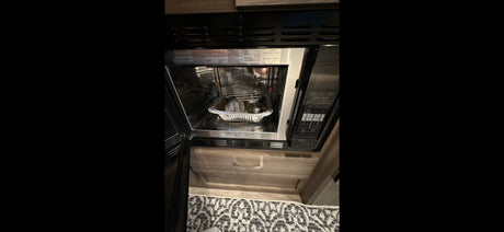 Inside an RV rental kitchen, a microwave contains a foil pan and metal rack, highlighting the compact cooking setup.