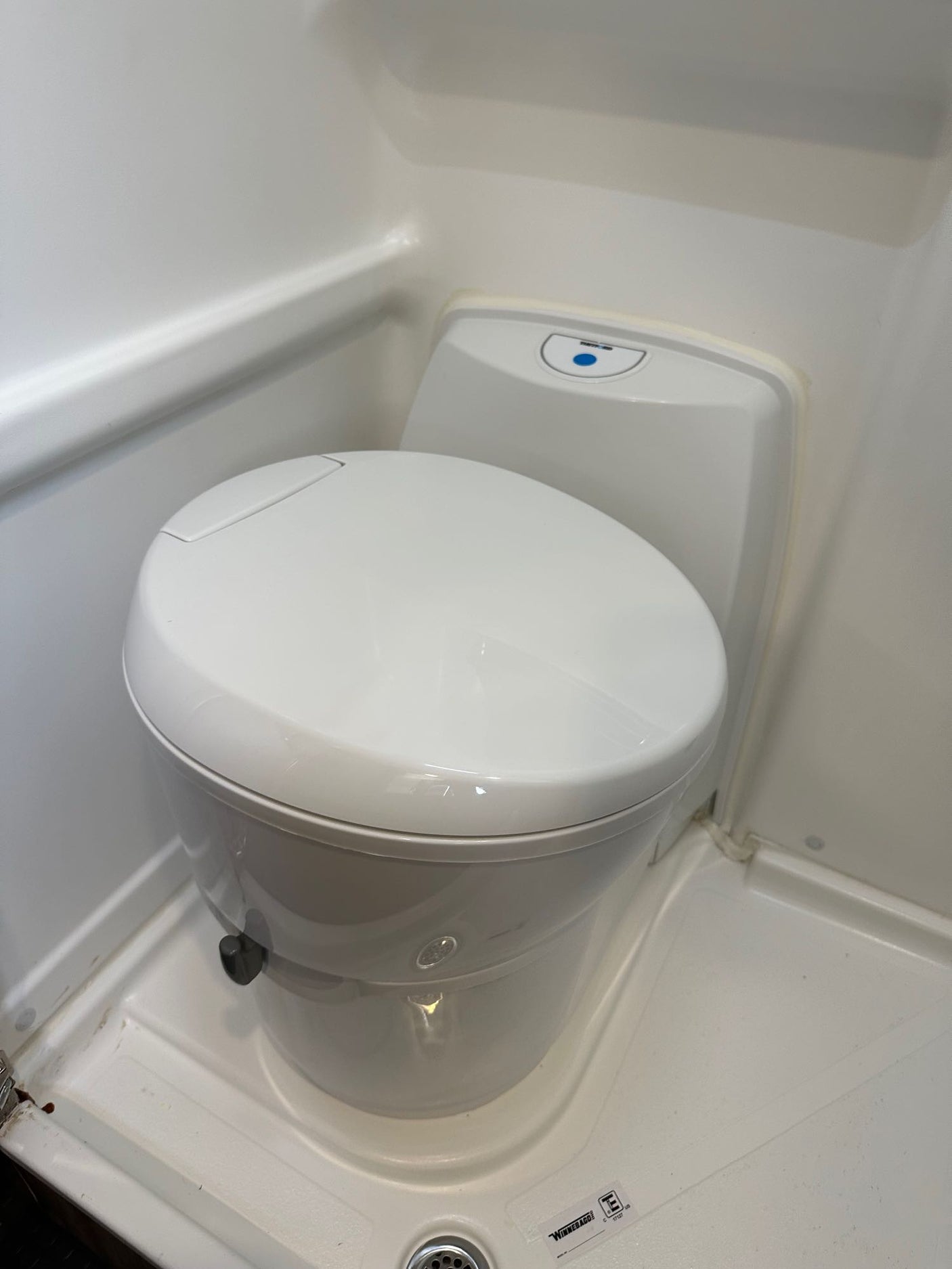 A white, compact toilet is shown in a small, molded RV rental bathroom, highlighting its space-saving design.