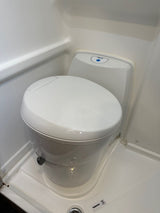 A white, compact toilet is shown in a small, molded RV rental bathroom, highlighting its space-saving design.