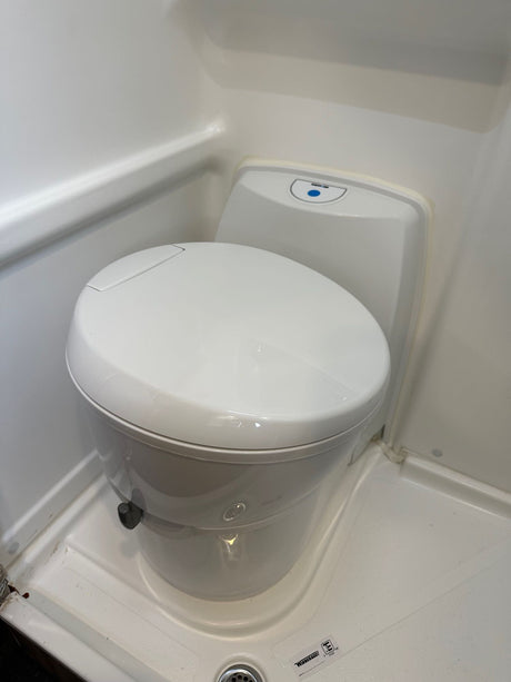 A white, compact toilet is shown in a small, molded RV rental bathroom, highlighting its space-saving design.