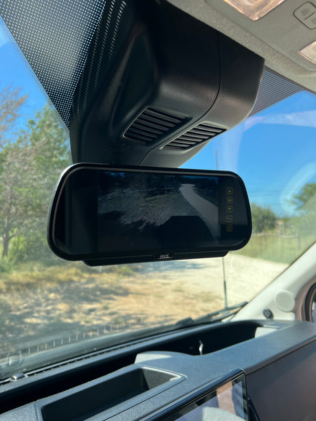 Inside an RV rental, the rearview camera monitor displays a dirt road view, essential for safe driving and maneuvering large vehicles.