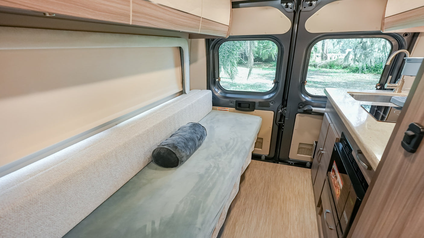Inside this RV rental: comfy bench seating, compact kitchen, and large rear windows showcasing the outdoors.