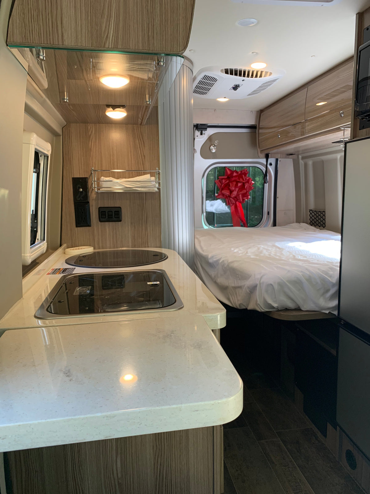 Bright, modern RV rental interior featuring a well-equipped kitchen area with a cooktop, and a spacious bed in the rear. — photo 18