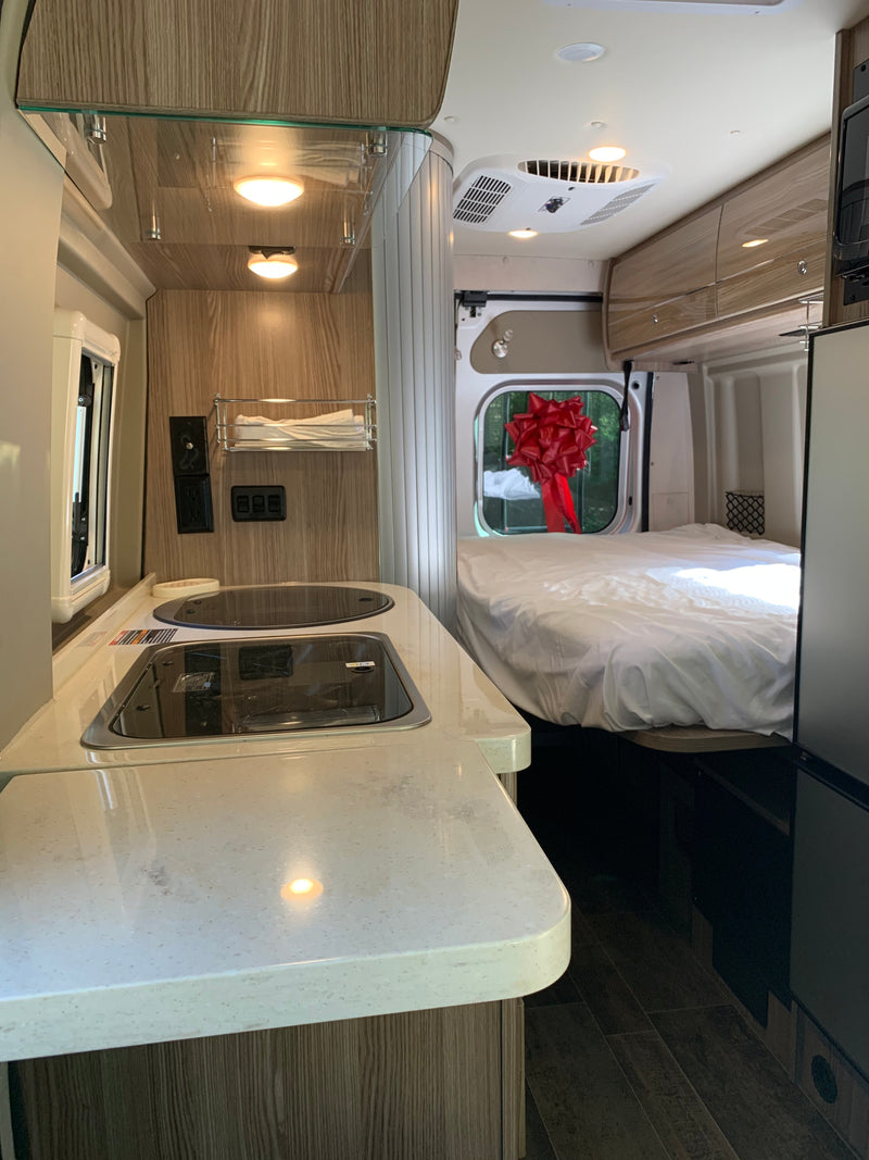 Bright, modern RV rental interior featuring a well-equipped kitchen area with a cooktop, and a spacious bed in the rear. — photo 18
