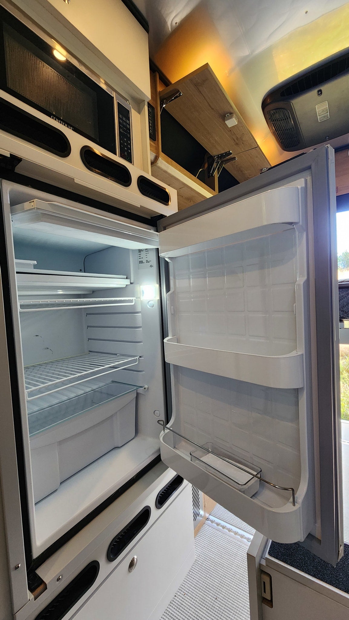 Open RV rental fridge and microwave showcase a functional camper kitchen setup. — photo 19