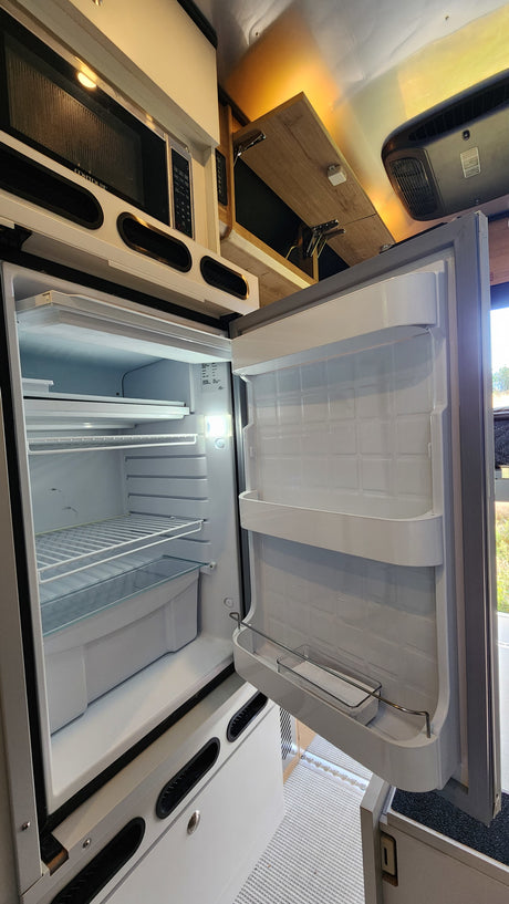 Open RV rental fridge and microwave showcase a functional camper kitchen setup.