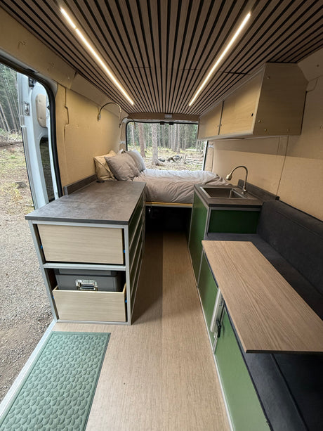 Inside a modern rv rental, featuring a comfortable rear bed, full kitchen, and flexible living space with wood accents.