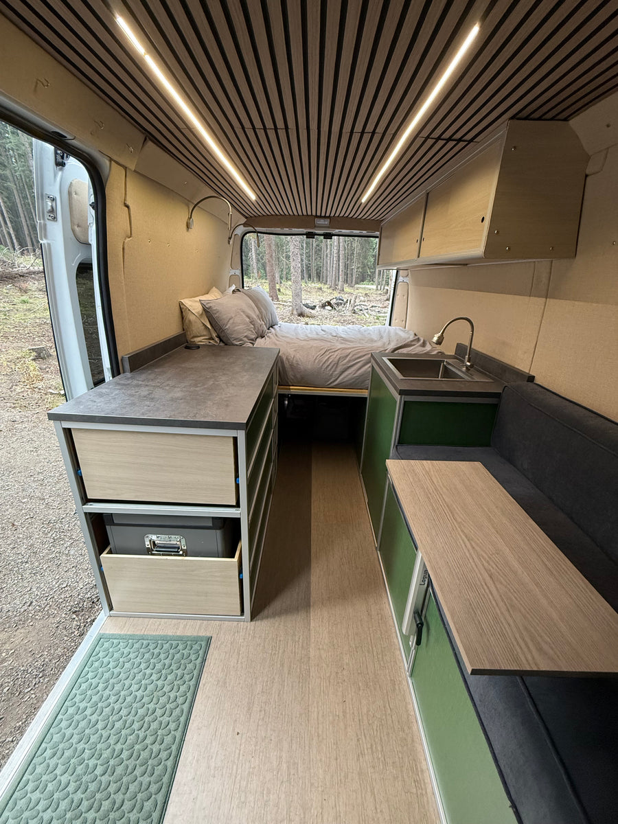 Inside a modern rv rental, featuring a comfortable rear bed, full kitchen, and flexible living space with wood accents.