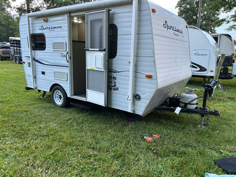 This white Sportsmen RV rental features an open door, propane tanks, and is parked on grass.
