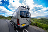 This Winnebago Revel Sprinter rv rental, parked on a scenic mountain road, offers stunning views of a green valley under a blue, cloudy sky.