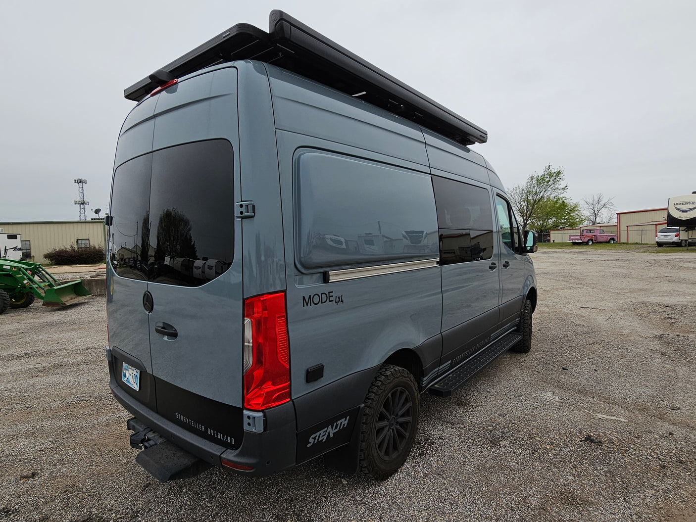 A grey Storyteller Overland 4x4 Sprinter camper van, featuring a roof awning and rugged tires, awaits your next rv rental journey.