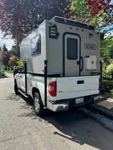 A white pickup truck with a Scout truck camper mounted in its bed, parked on a street. This RV rental is ready for adventure.