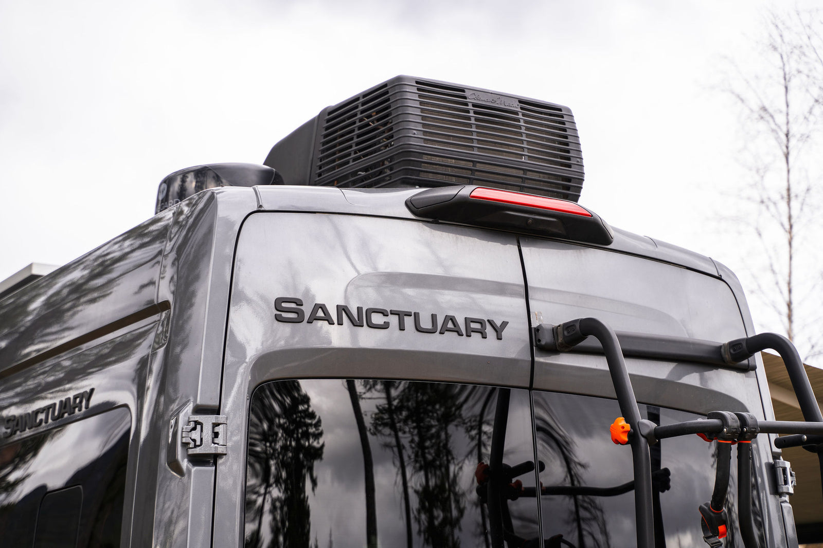 Close-up of a gray Sanctuary RV rental's rear, featuring a rooftop AC unit and a bike rack for your next adventure.