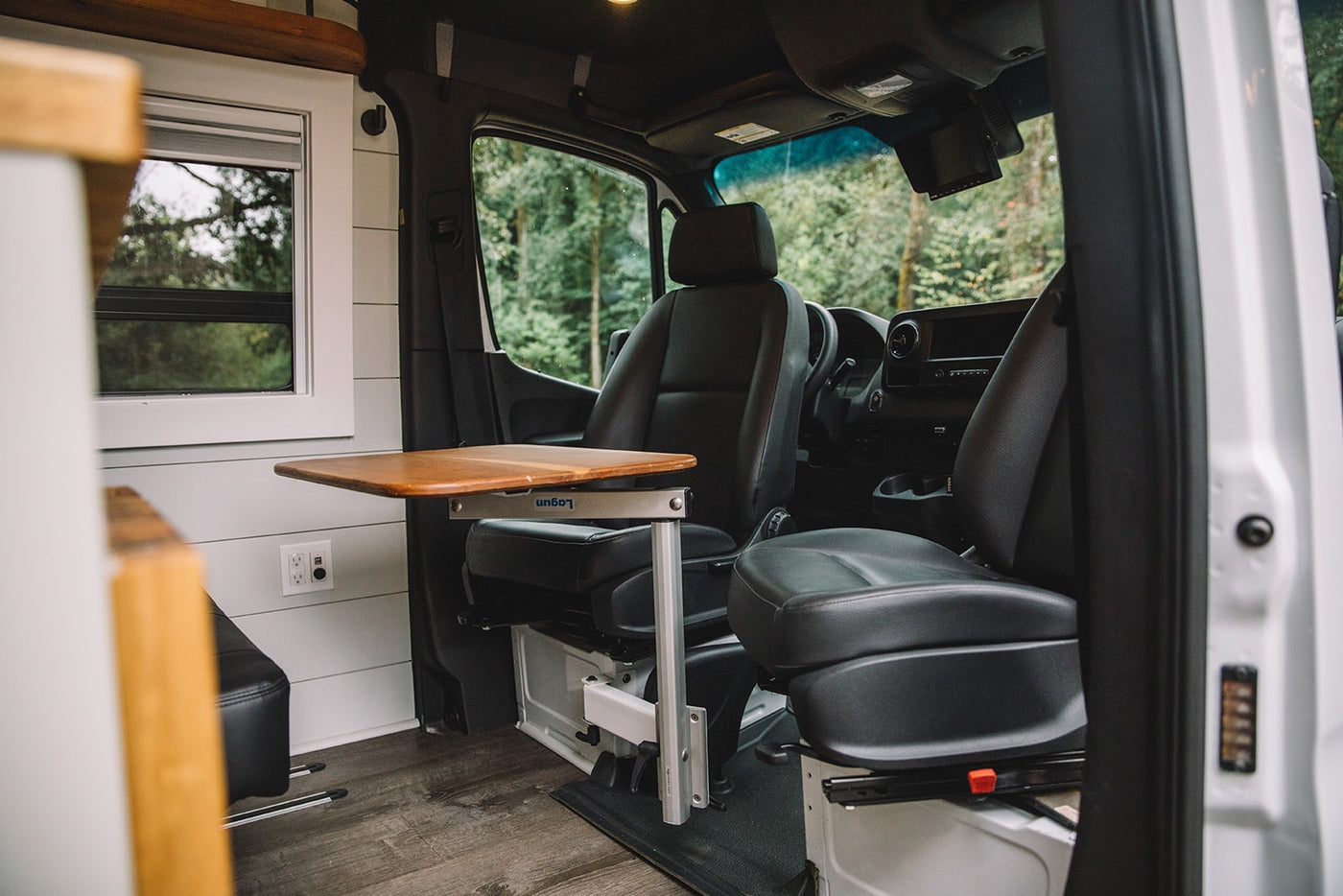  parked in a treed natural setting.|White custom camper van with open sliding door showcasing its cozy interior — photo 6